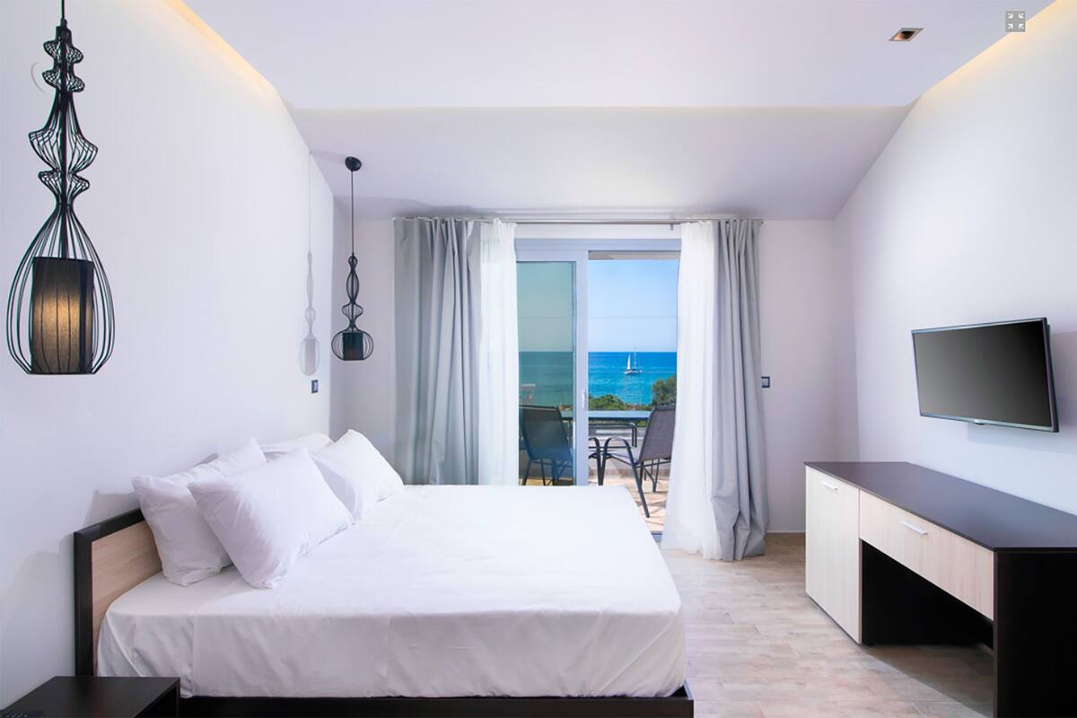 Une chambre d’hôtel équipée d’un lit, d’un bureau, d’une télévision et d’un balcon avec vue sur la mer.