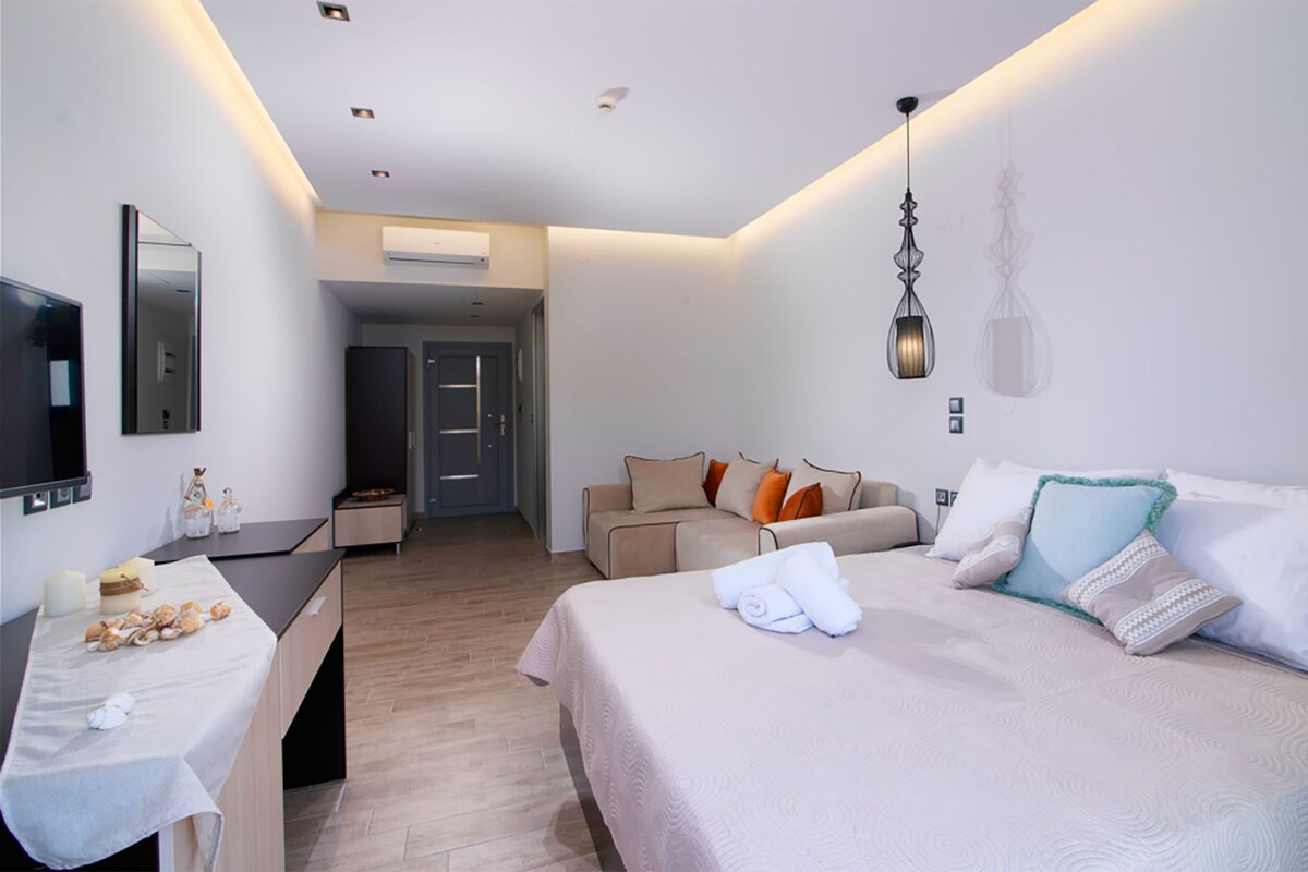 Een hotelkamer met een bed, een bureau, een televisie, een bank en een deur naar een gang.