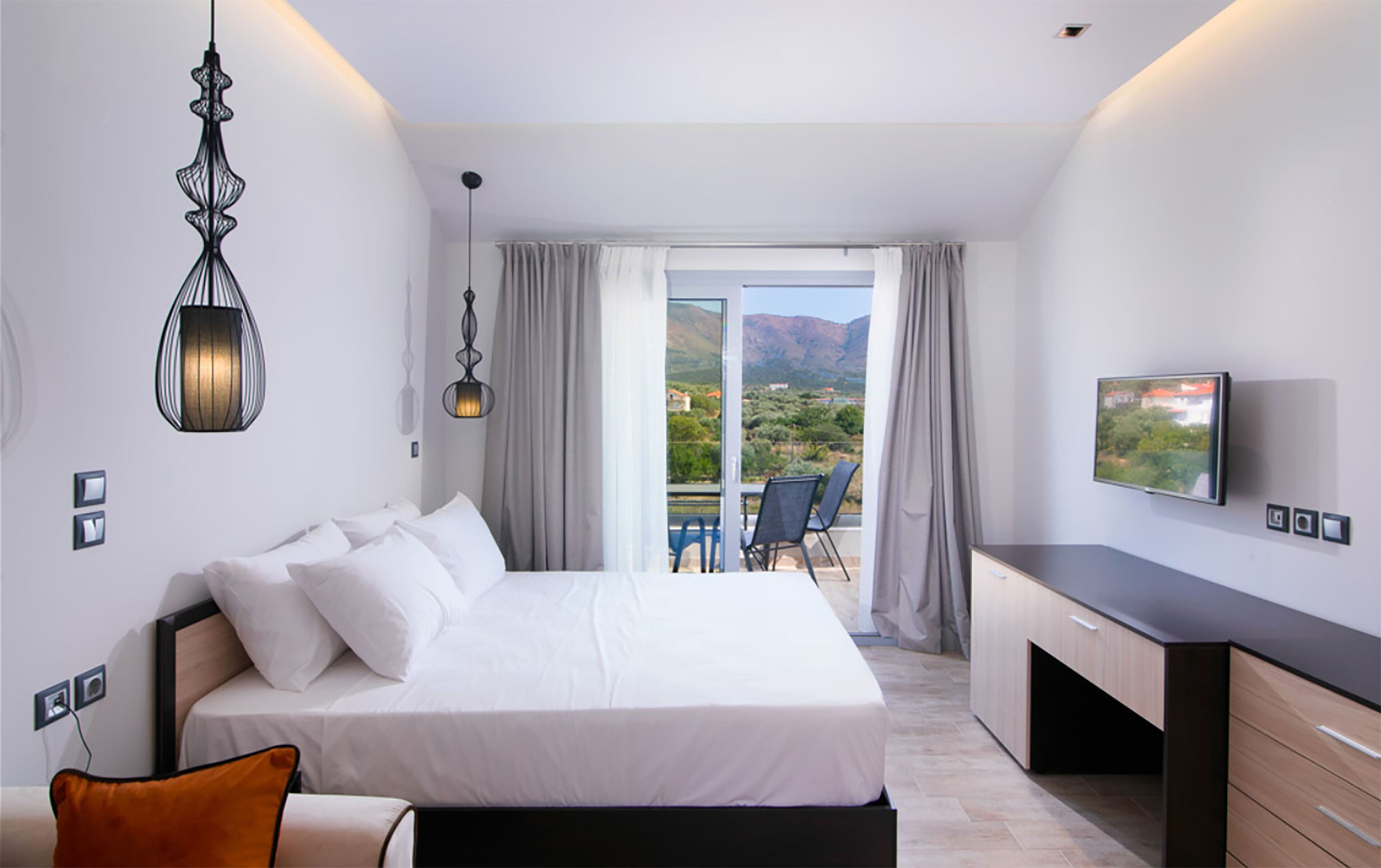 A hotel room with a bed, a desk, a TV, and a balcony with a view.