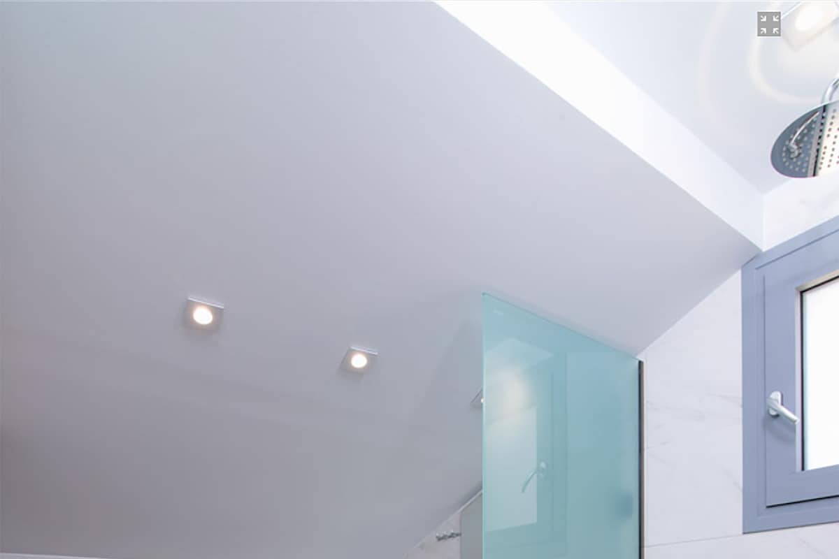 Un baño con inodoro, cabina de ducha de vidrio, pared con azulejos de mármol e iluminación empotrada en el techo.