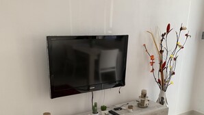 A modern living room with a flat-screen TV mounted on a wall, a wooden console table with decorative items, and a red rug on the floor. - Holiday House Partanna Mondello (Mondello)