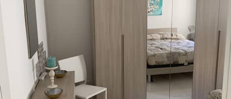 Un dormitorio con cama, armario, escritorio y silla.