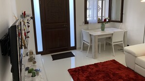 A modern living room with a white sofa, a dining table with two chairs, a red rug, a TV, and a large mirror. - Holiday House Partanna Mondello (Mondello)