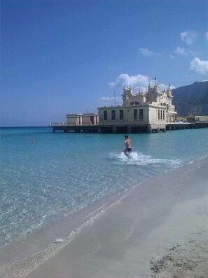 Una spiaggia con acque cristalline turchesi, un molo e un grande edificio con numerose torri.
