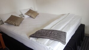 Ein ordentlich bezogenes Bett mit weißen Leinentextilien, zwei Kissen und einer grauen Decke.