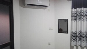Eine weiße Wand mit montiertem Klimagerät, einem kleinen gerahmten Spiegel und einer Steckdose.