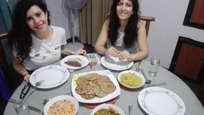 Zwei Personen sitzen an einem runden Esstisch mit verschiedenen Speisen, darunter Fladenbrote, Reis und ein Salat.