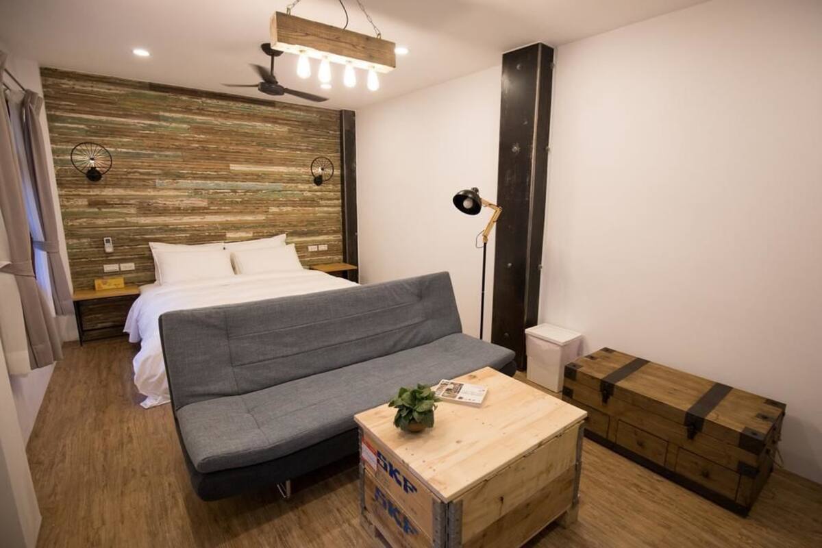A bedroom with a bed, grey sofa, wooden coffee table, and a chest of drawers.