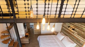 Un dormitorio moderno con cama estilo loft, suelo de madera y un diseño de techo único con lámparas colgantes.