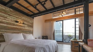 Un dormitorio con una cama grande, vigas de madera en el techo, techo inclinado y vistas al exterior a través de un ventanal.