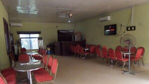A dining area with red chairs and tables, a fan, and a TV on the wall. - Keblat Hotel  Suites (Abeokuta)