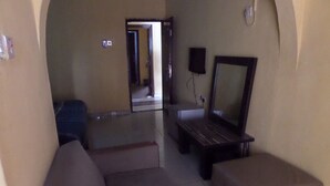 A room with a sofa, ottoman, and a large mirror on the wall. - Keblat Hotel  Suites (Abeokuta)