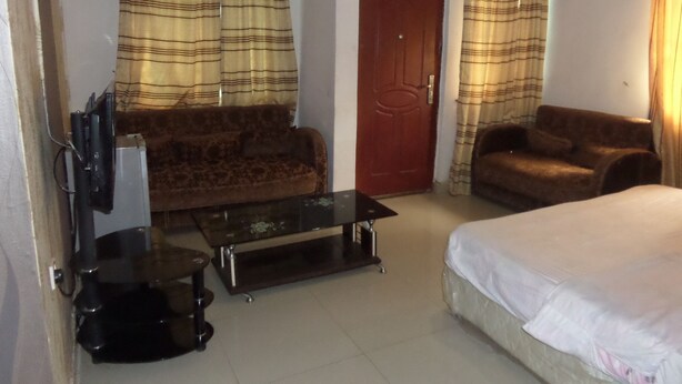 A room with a sofa, a bed, a coffee table, and curtains. - Keblat Hotel  Suites (Abeokuta)