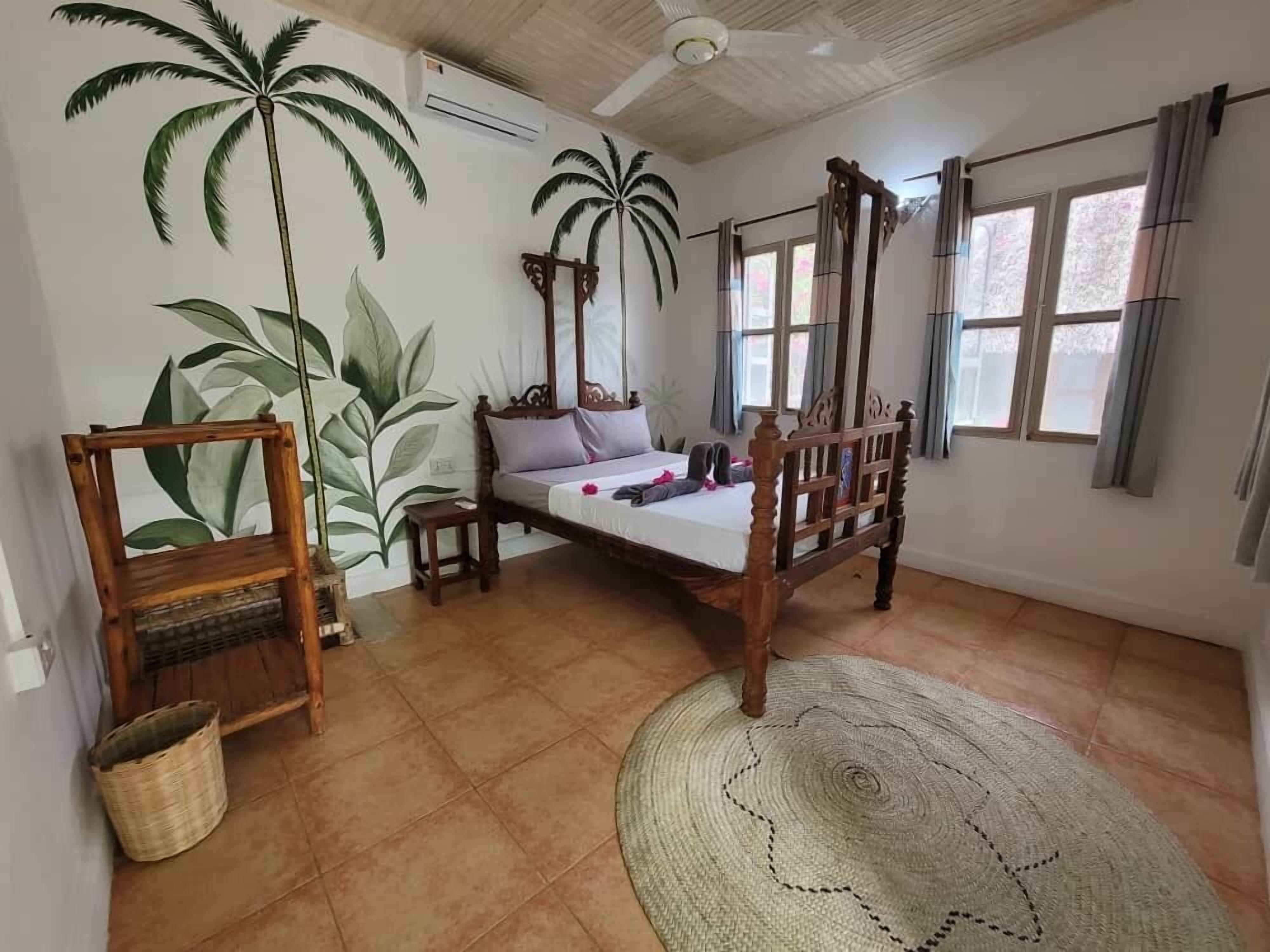 A bedroom with a wooden bed, a woven rug, and wall art of palm trees.