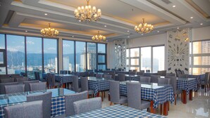 A restaurant with tables covered in blue and white checkered tablecloths, grey upholstered chairs, and chandeliers.