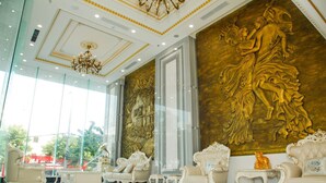 A luxurious lobby with ornate gold wall art, elegant white furniture, and a grand chandelier.