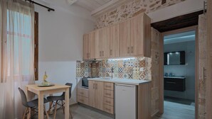 Une cuisine de taille réduite, dotée de meubles de rangement en bois, d’un crédence carrelée, d’une petite table à manger avec des chaises et d’un réfrigérateur.