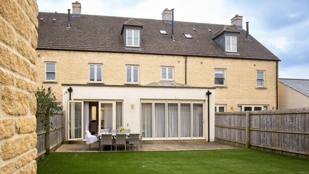 Une maison en pierre à deux étages, dotée d’une cour arrière clôturée, d’une terrasse avec mobilier d’extérieur et d’une véranda.