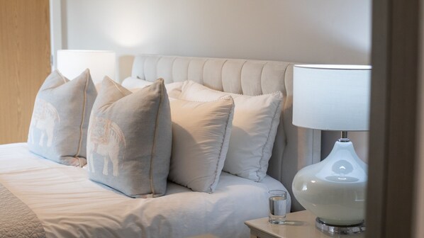 A neatly made bed with a white duvet and several pillows, a bedside table with a lamp, and a glass of water.