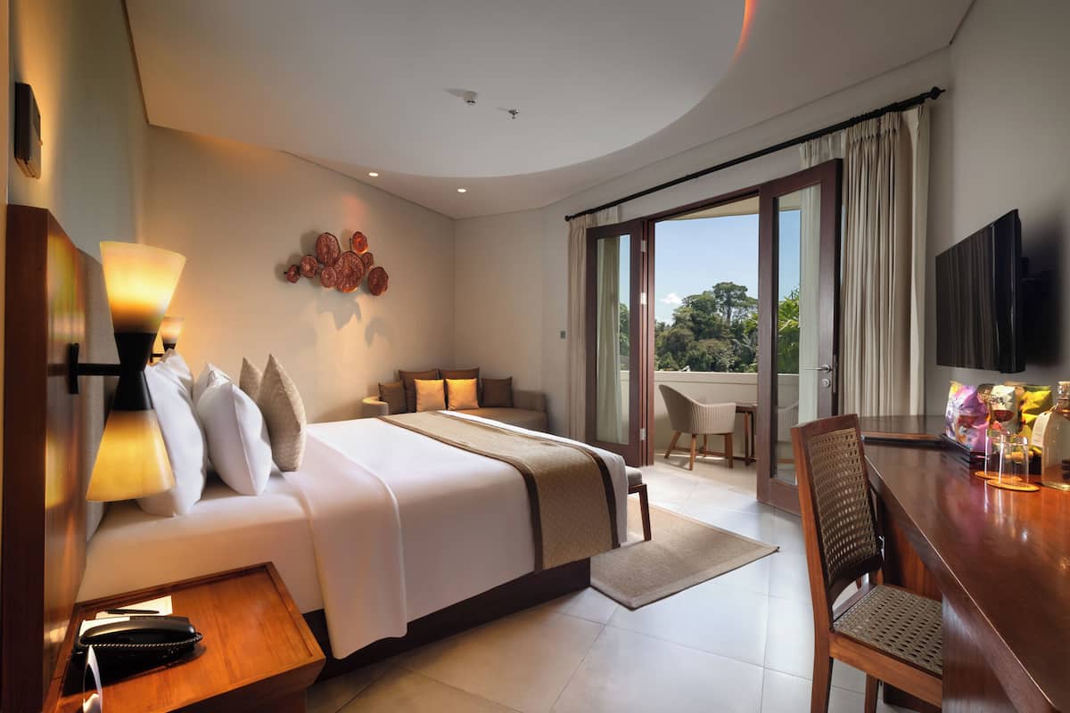 A modern hotel room with a large bed, a desk, a chair, a balcony with a view, and a flat-screen TV.