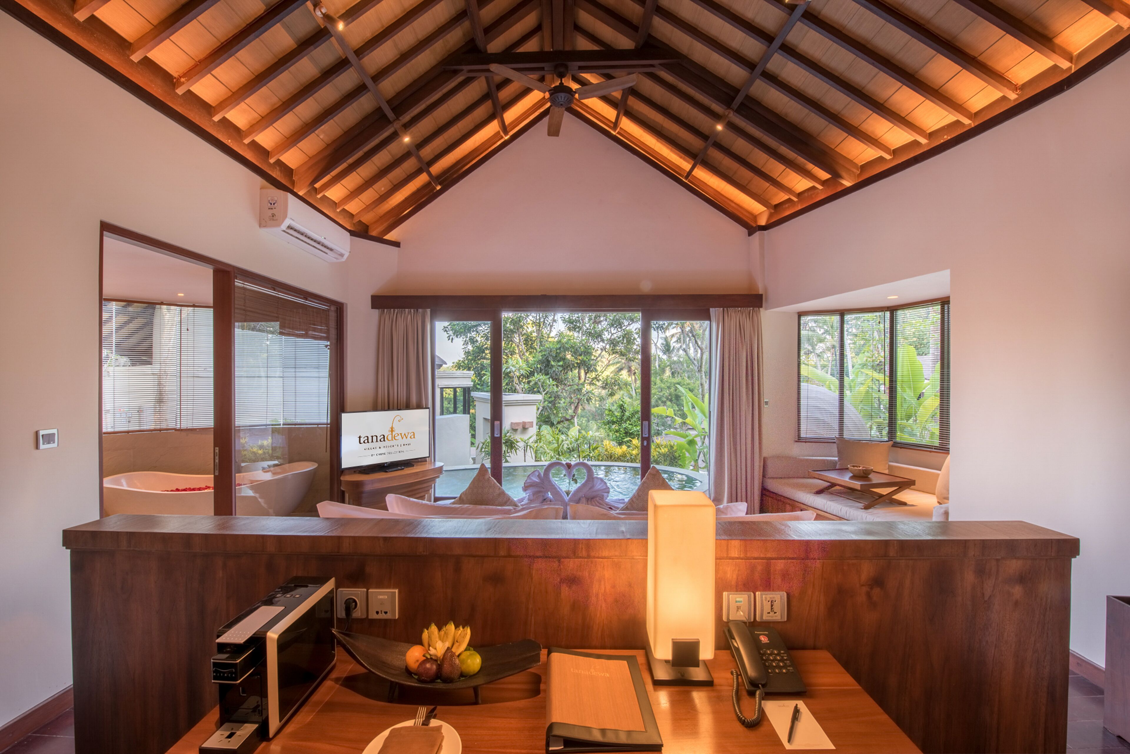 A reception area with a wooden reception desk, a digital screen, a bathtub, and a view of the outdoors.