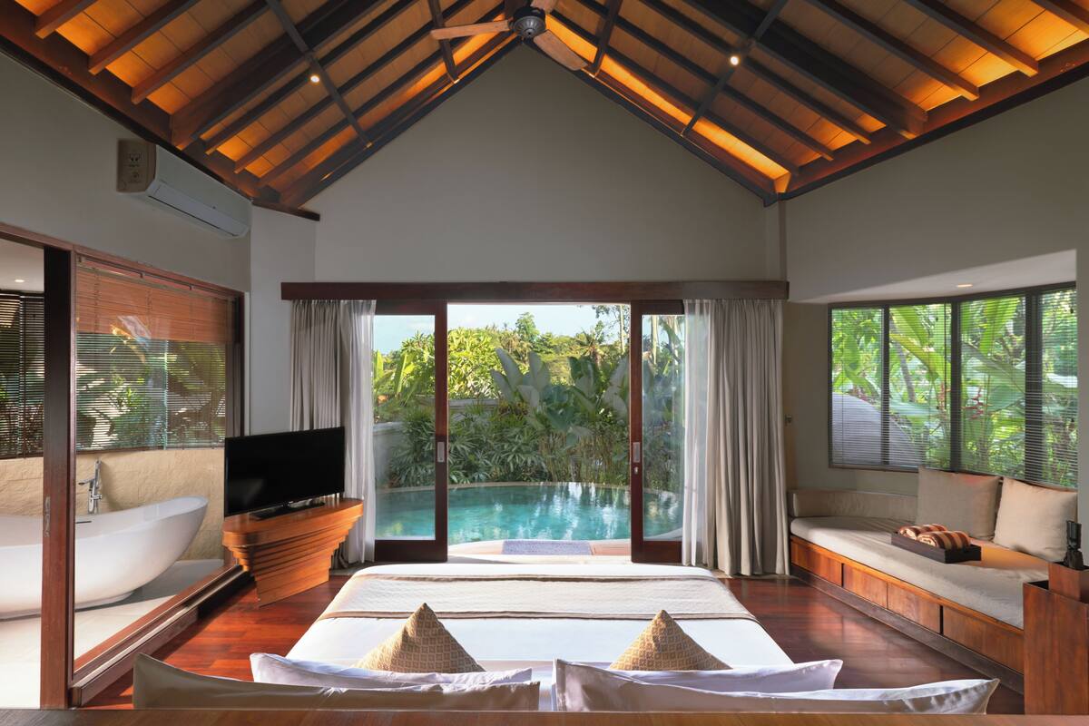 A bedroom with a large bed, a TV, a bathtub, and a view of a swimming pool.