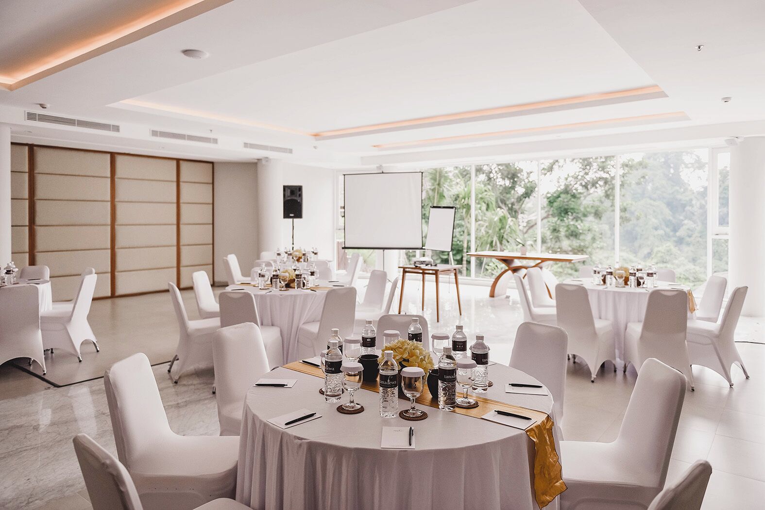 A conference room with round tables, white chairs, and a projector screen.