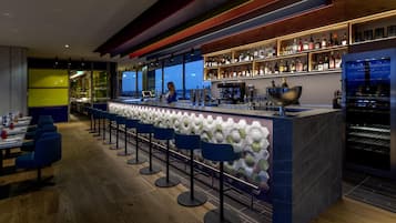 A modern bar area with a bartender, bar stools, and shelves of liquor bottles.