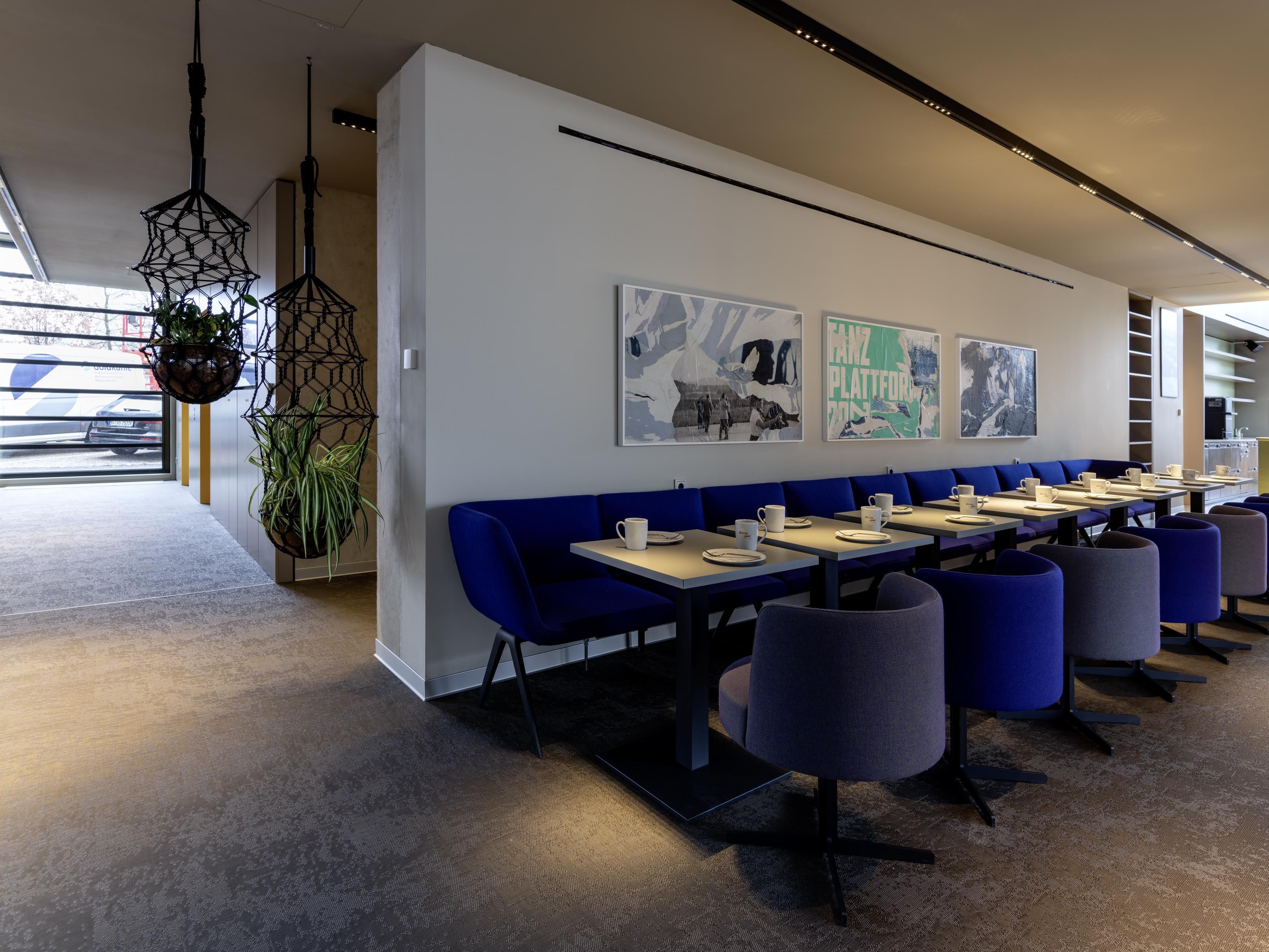 A modern restaurant with blue seating, hanging plants, and artwork on the walls.