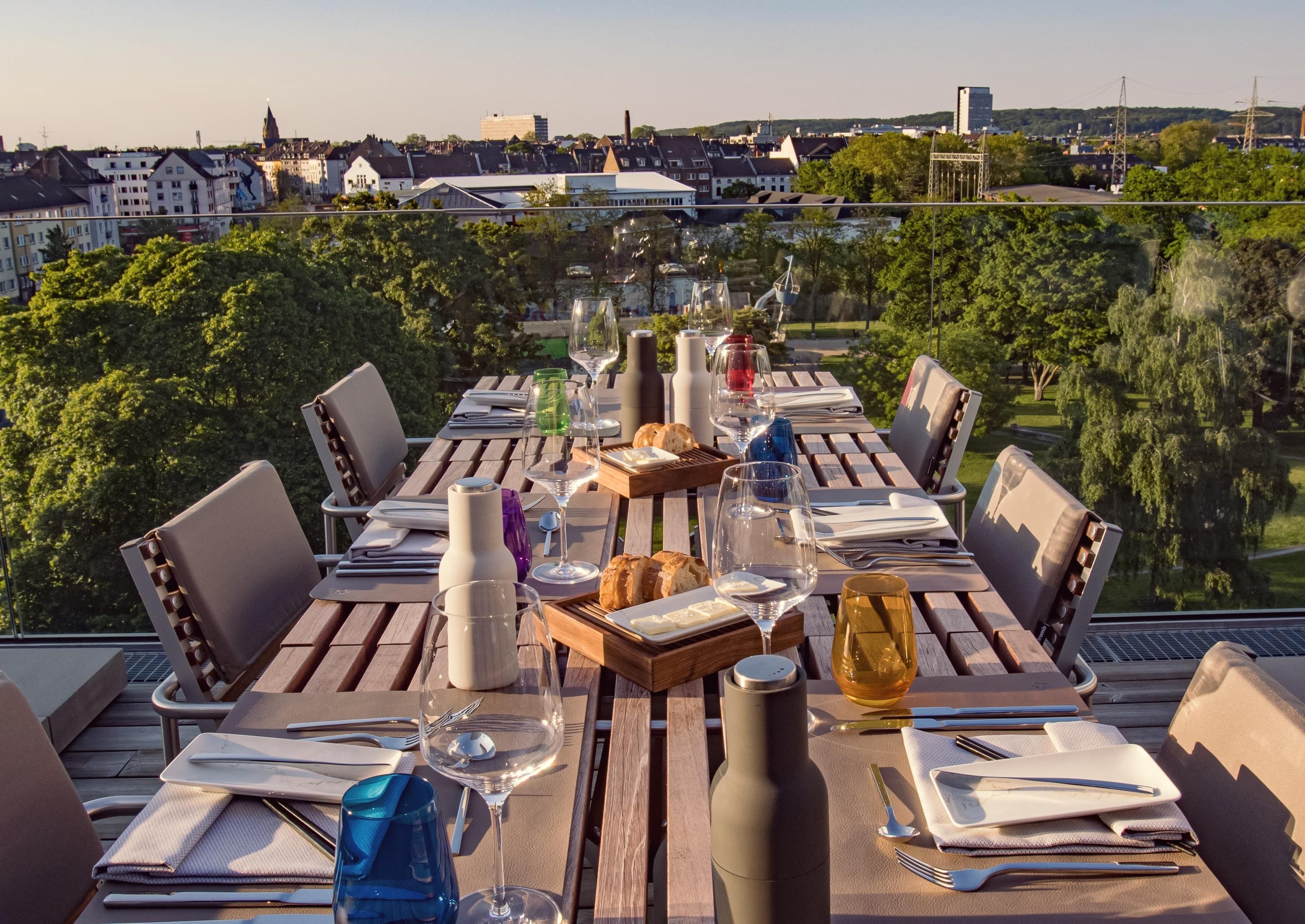 Une table à manger dressée pour six personnes, avec vue sur la ville, des sièges d’extérieur et un assortiment de vaisselle et de verrerie.