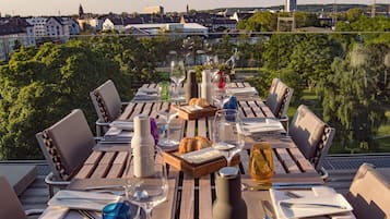 Une table à manger dressée pour six personnes, avec vue sur la ville, des sièges d’extérieur et un assortiment de vaisselle et de verrerie.