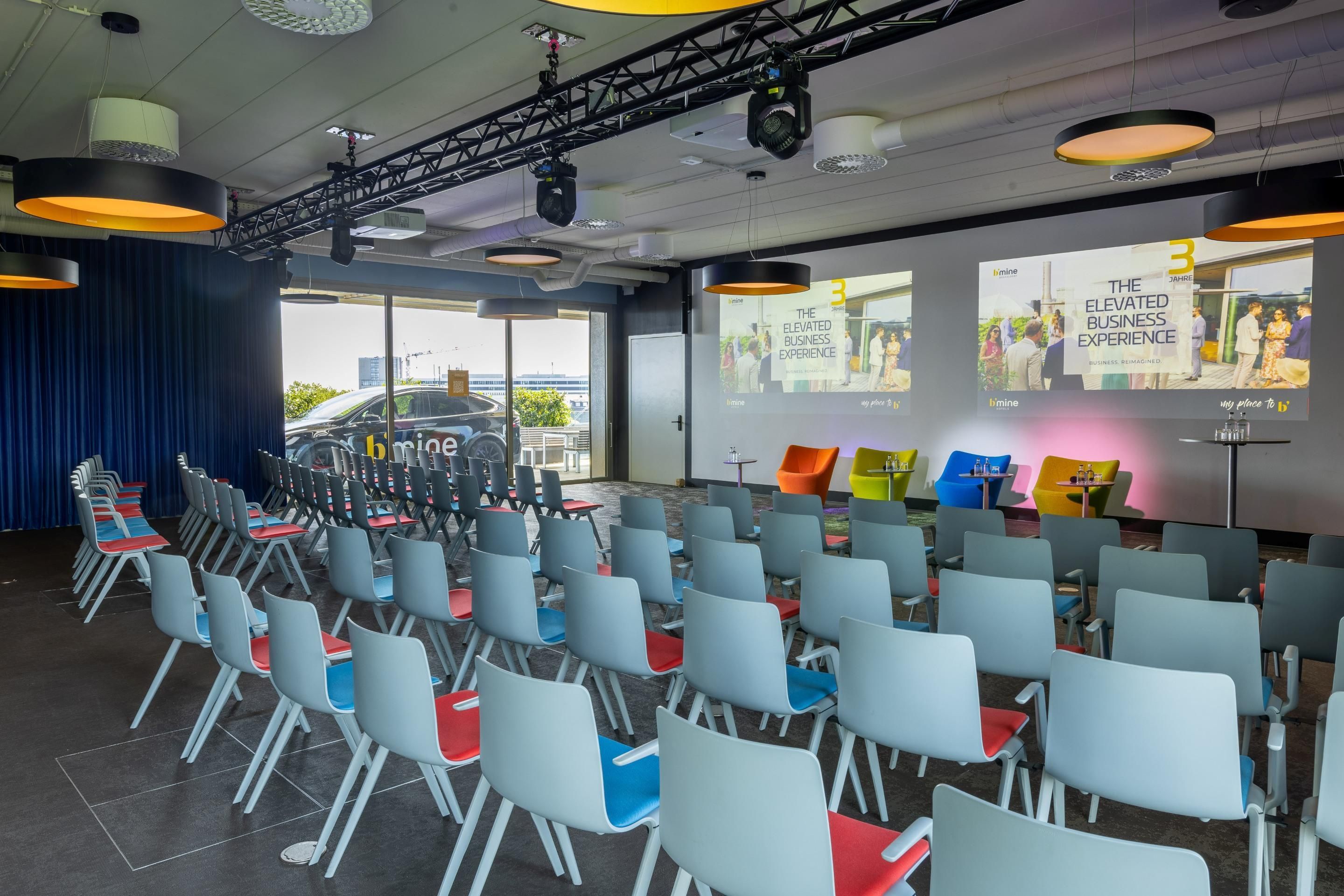 Une salle de conférence avec des rangées de chaises, une scène équipée d’un système d’éclairage et un écran de projection affichant un thème lié à l’expérience en entreprise.