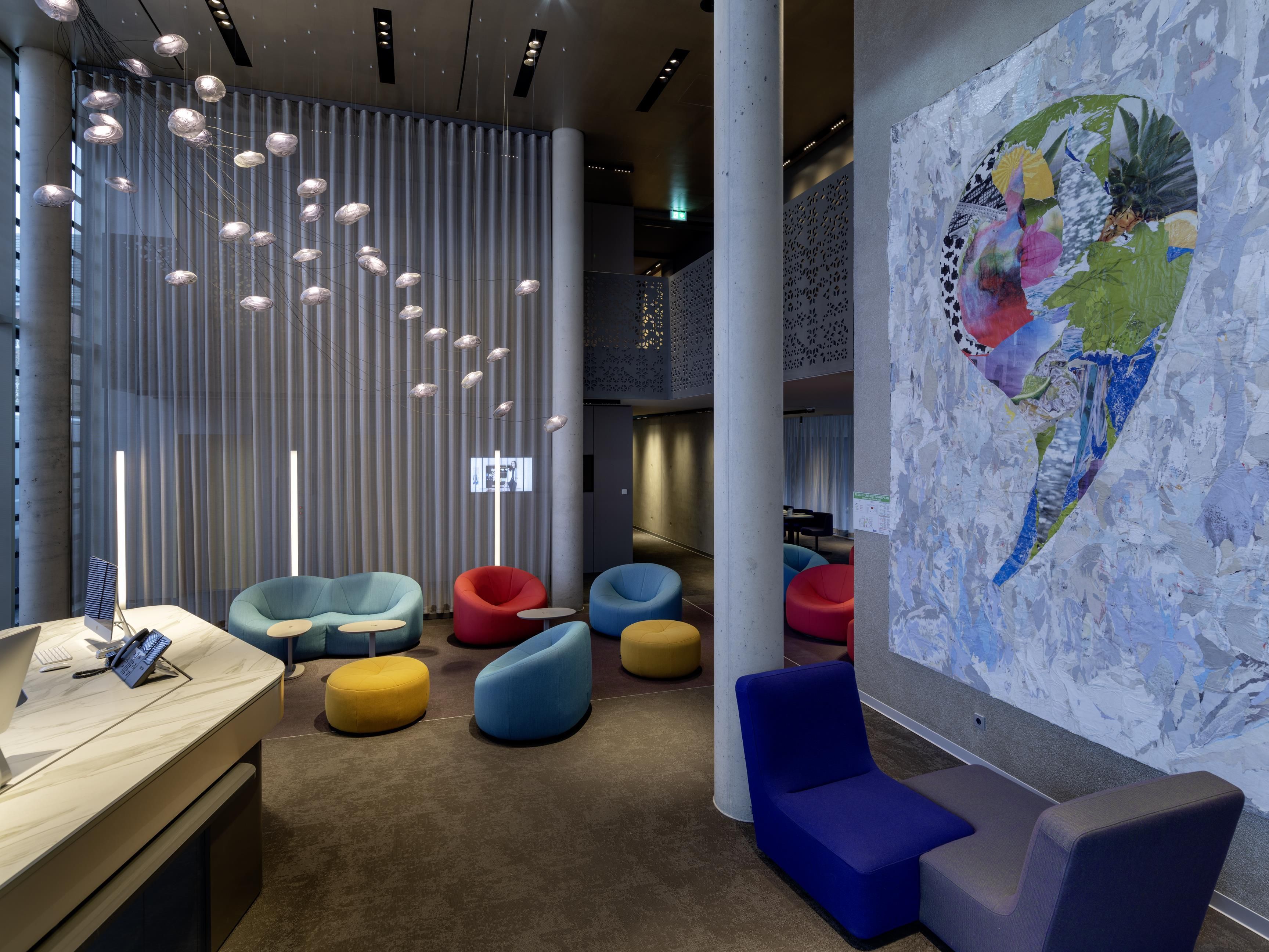 A modern interior with a reception desk, colorful seating, a large abstract mural, and a vertical light installation.