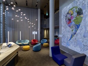 A modern interior with a reception desk, colorful seating, a large abstract mural, and a vertical light installation.