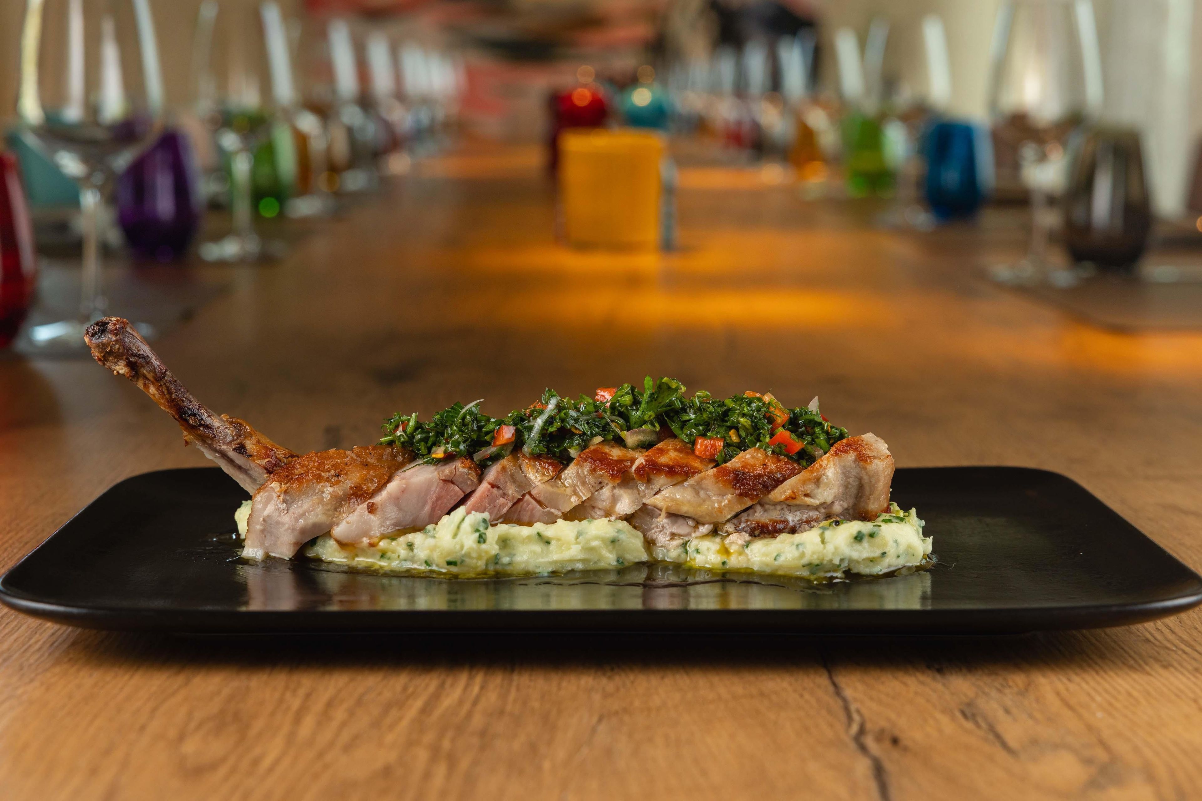 A dish with a roasted leg of lamb on a black plate.