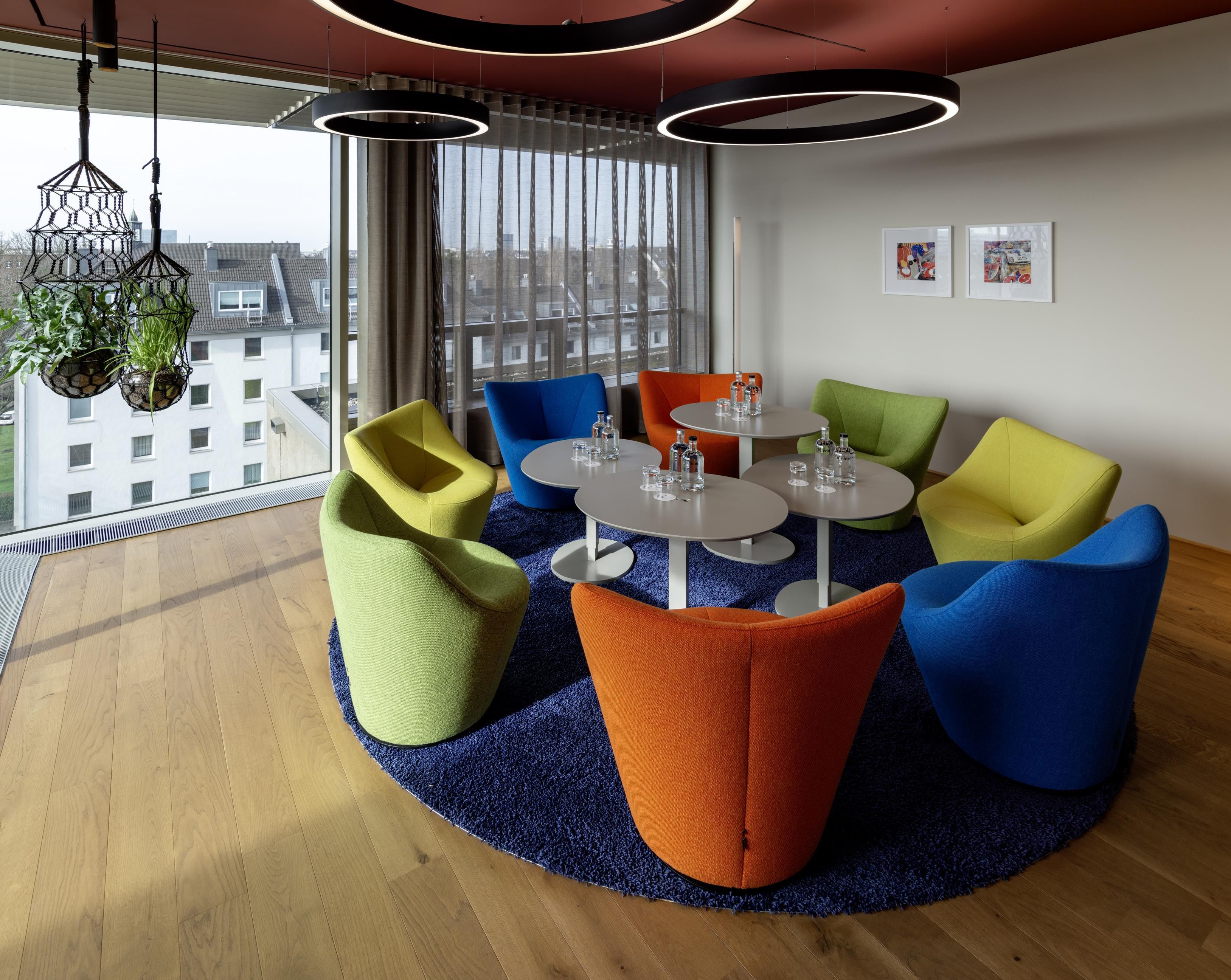 A modern lounge area with colorful seating, a round table, and a city view.