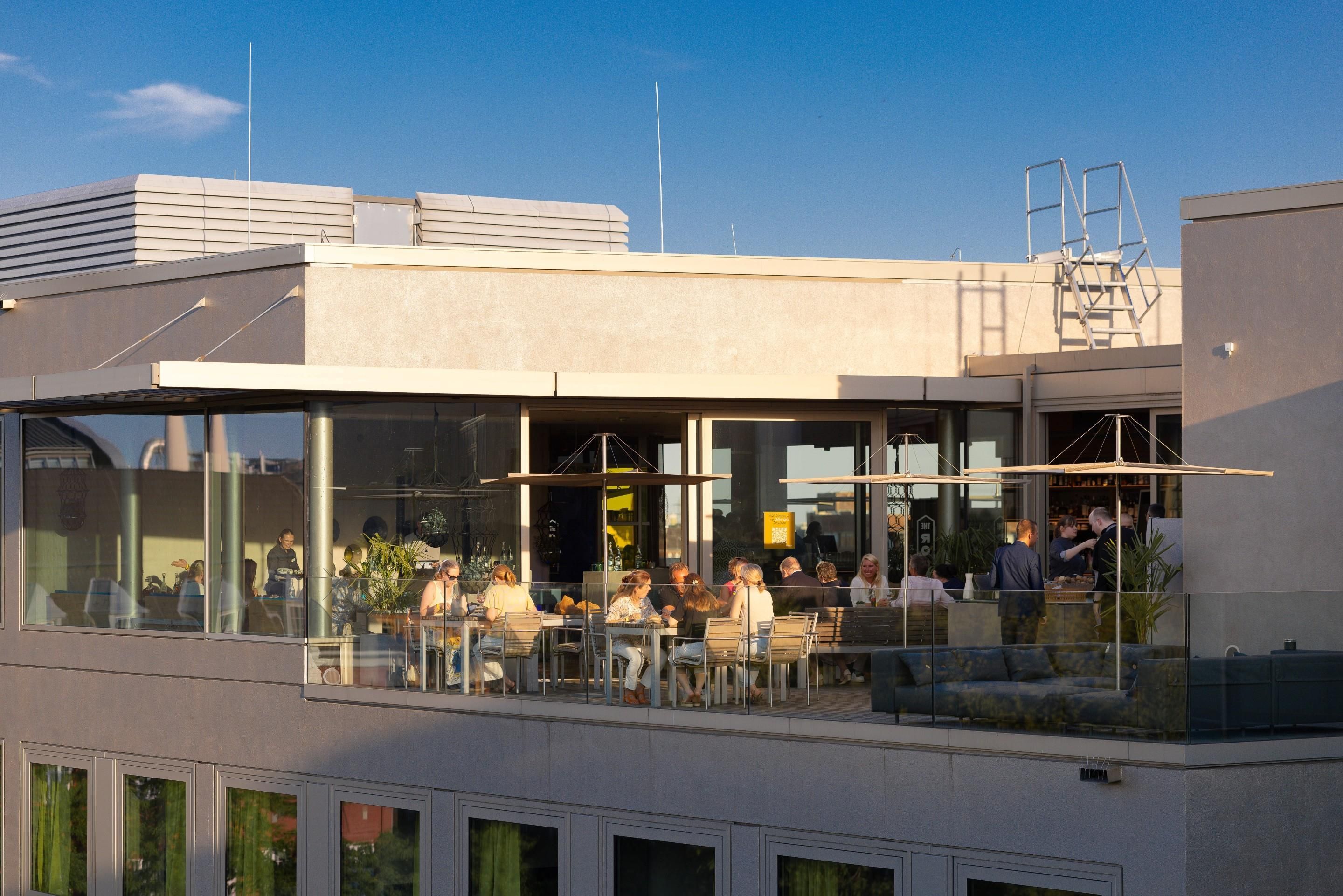 A modern building with a rooftop dining area, large windows, and a visible staircase.