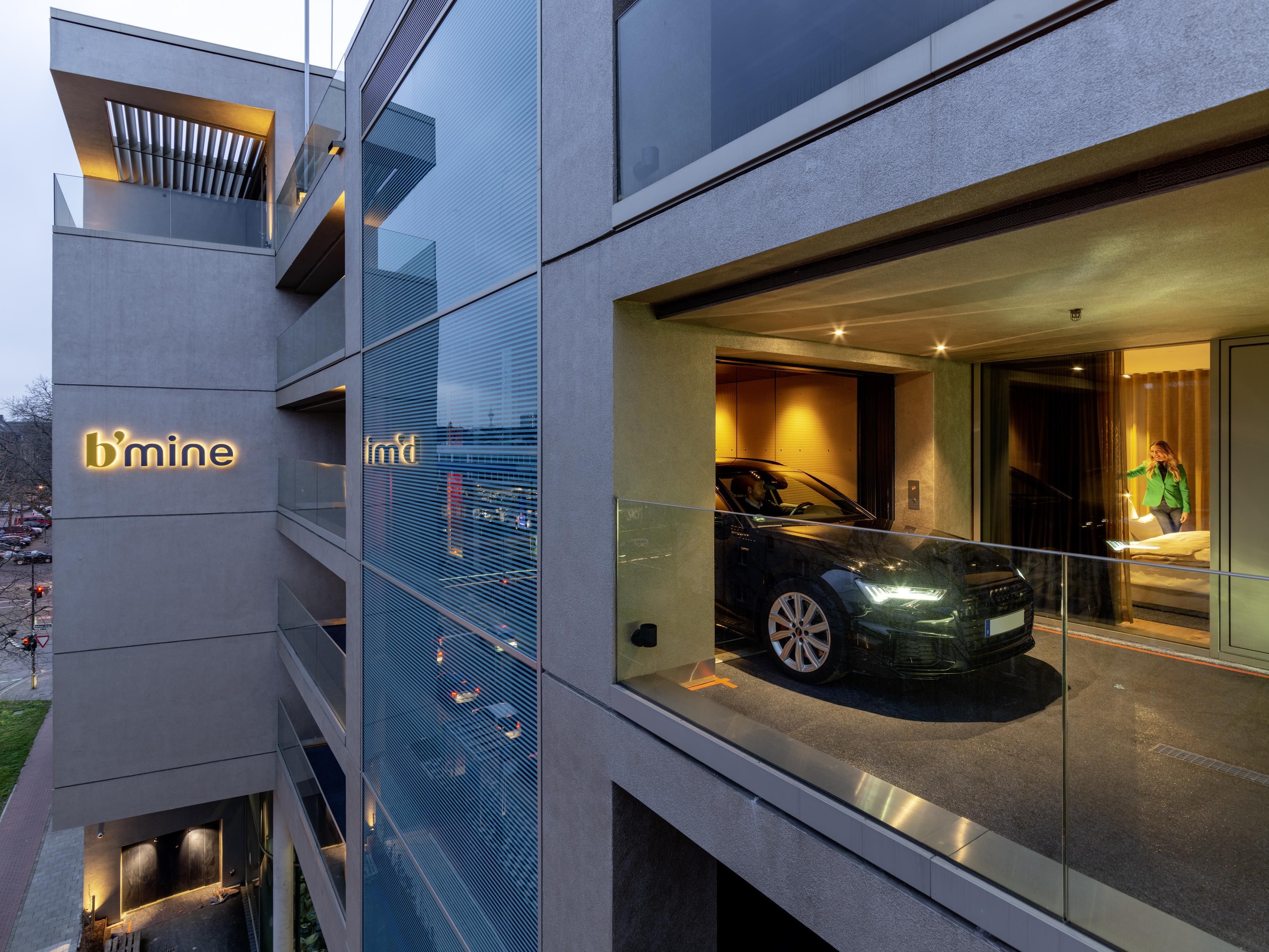 A modern building with a glass facade, a car displayed outside, and a visible entrance.