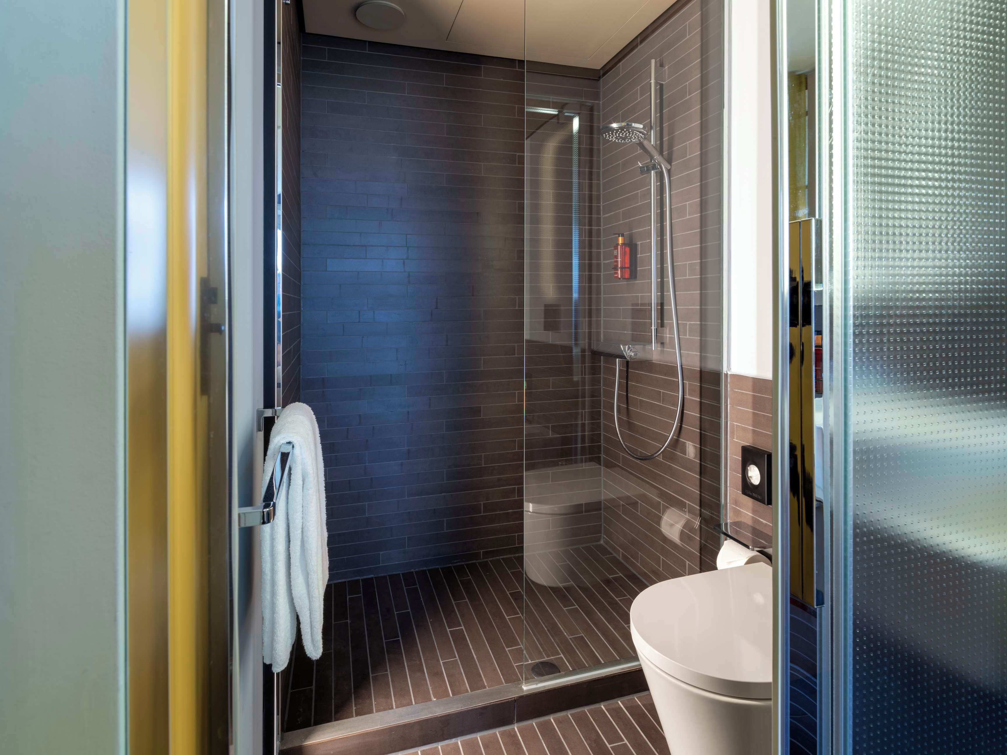 Une salle de bain moderne avec une douche à parois de verre, des toilettes blanches et une serviette suspendue à un porte-serviettes.