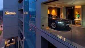 Een modern gebouw met een glazen gevel, een auto in de etalage en het bord 'b'mine'.