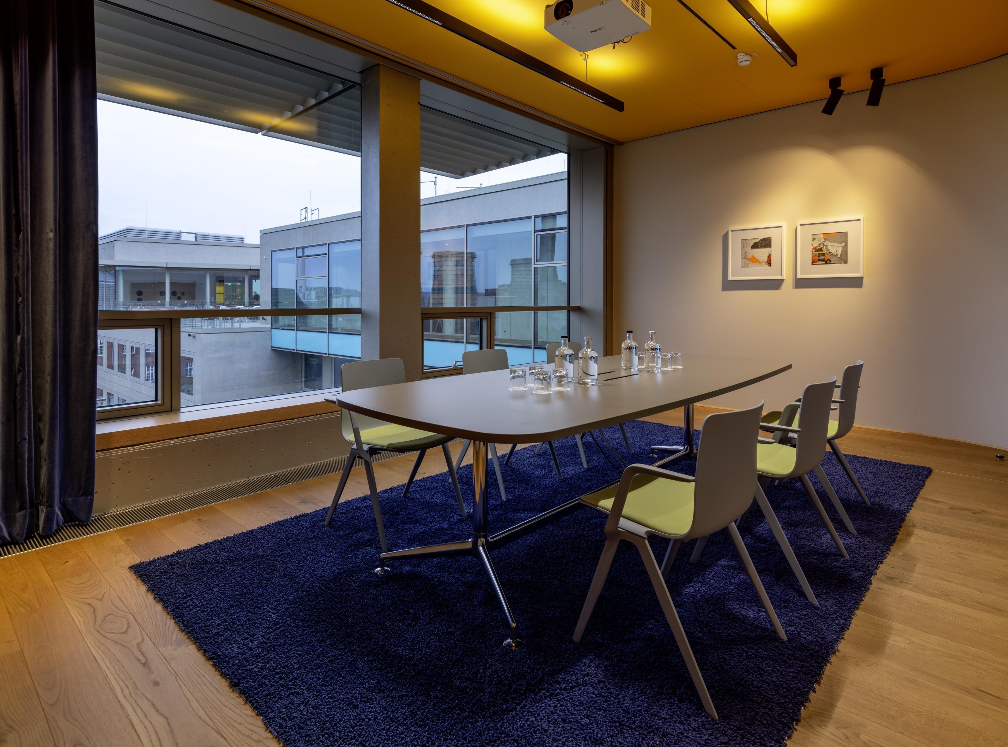 A conference room with a large table, chairs, a projector, and artwork on the wall.