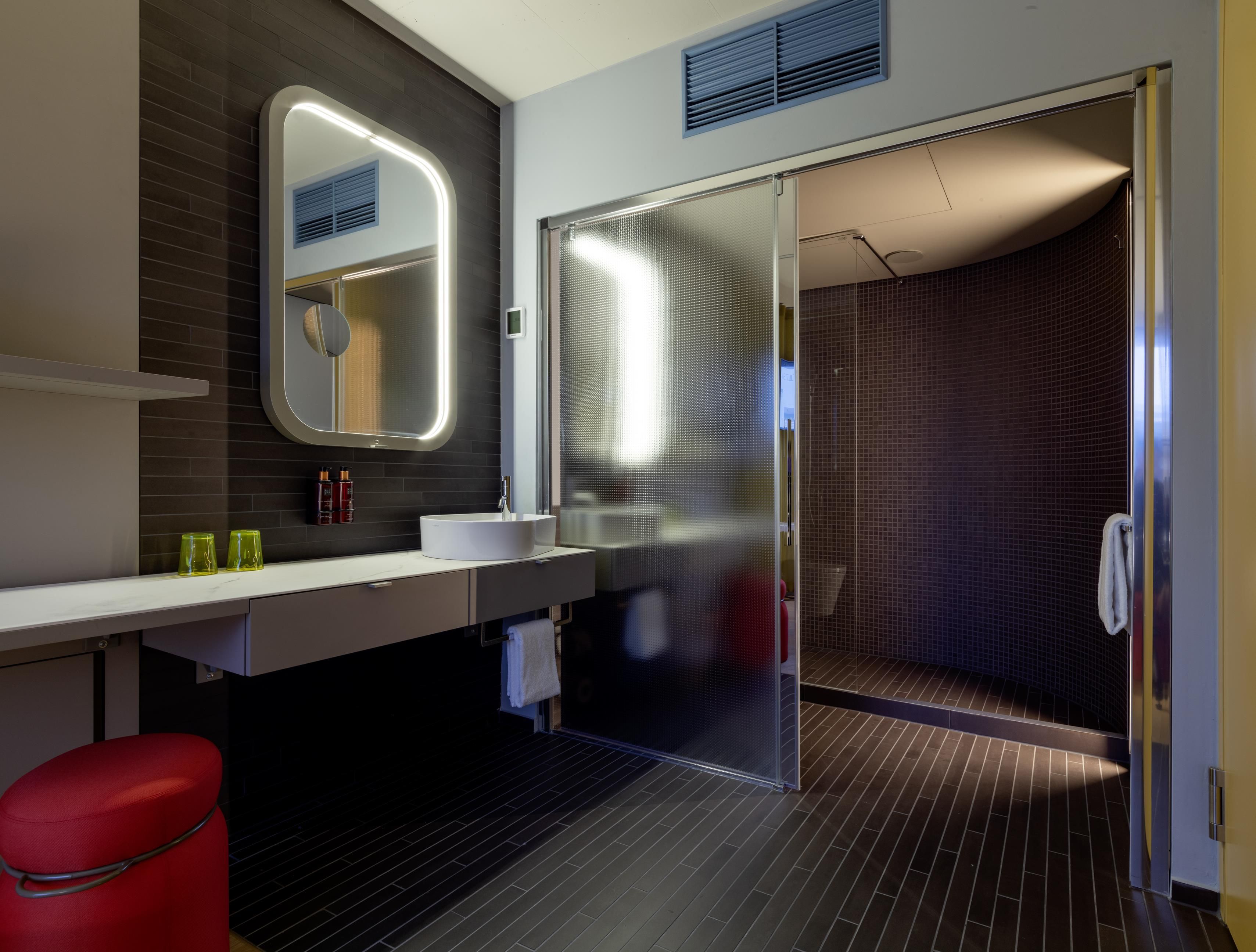 A modern bathroom with a large mirror, a round sink, and a shower area.
