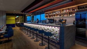 Een moderne bar met een lange toonbank, barstoelen en flessenrekken vol drank.
