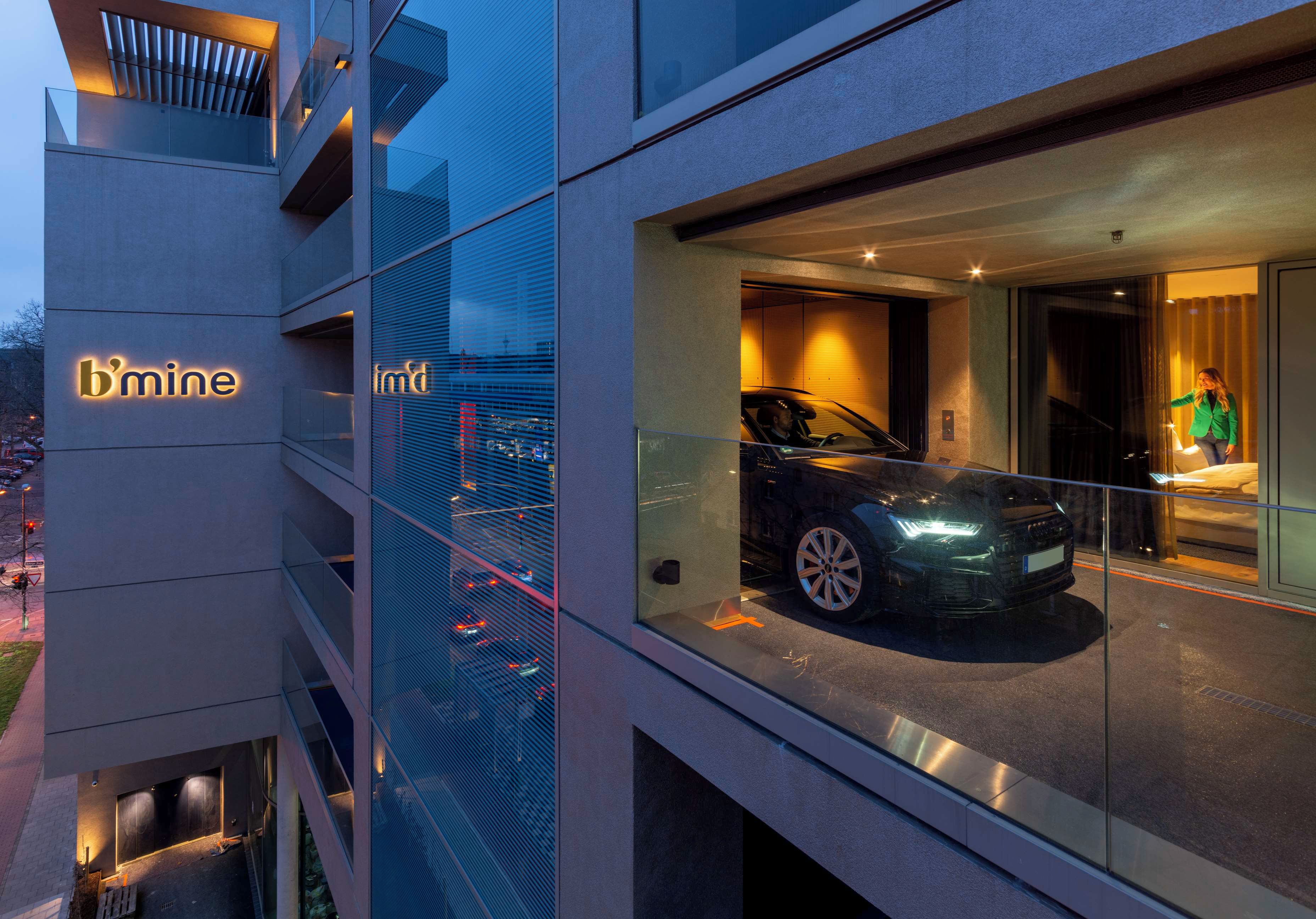 A modern building with a glass facade, a car displayed in the window, and the sign 'b'mine'.