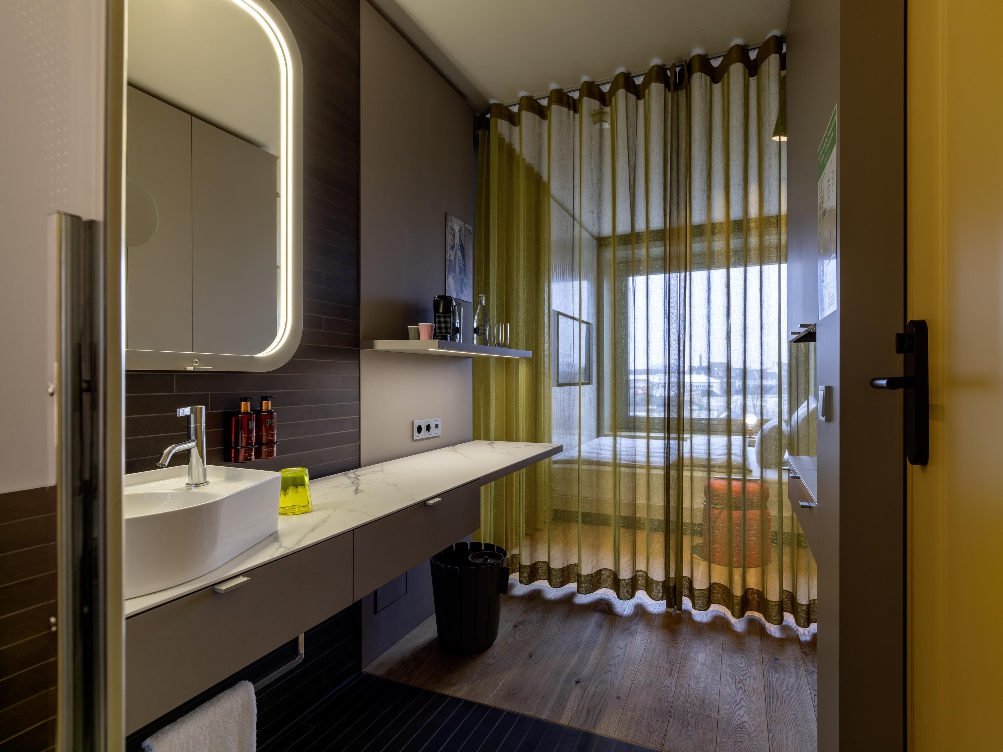 A modern bathroom with a large mirror, a sink, and a toilet. There is a window with a view of the city.