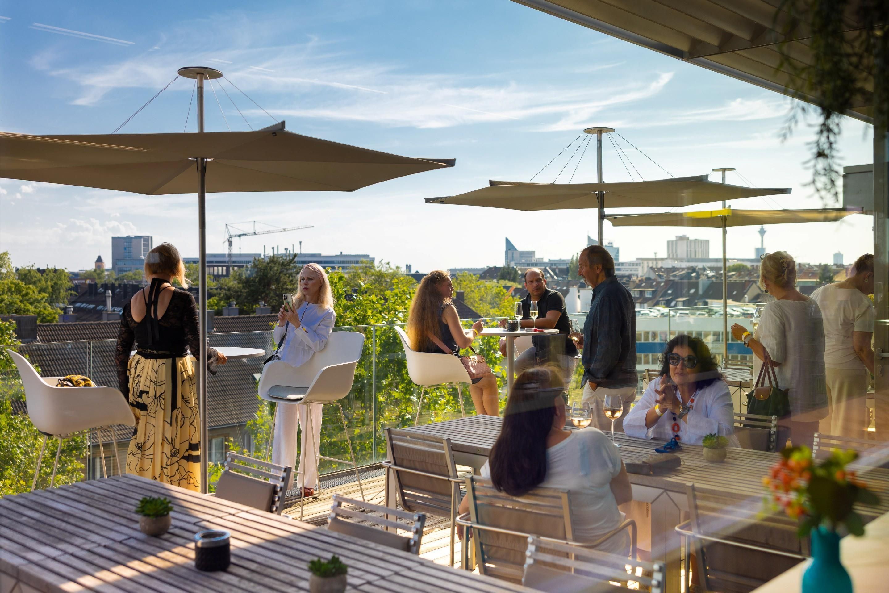 An outdoor dining area with tables and chairs, large umbrellas, and a view of the cityscape.