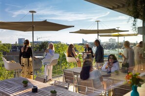 An outdoor dining area with tables and chairs, large umbrellas, and a view of the cityscape.