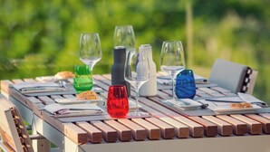 Une table en bois, ornée de différents verres et assiettes, est disposée à l’extérieur, avec un arrière-plan verdoyant flou.