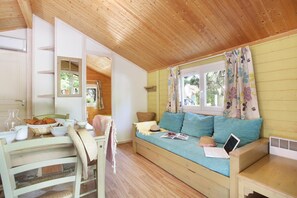 A cozy room with a wooden ceiling, a sofa with cushions, a dining table with breakfast items, and a window with curtains.