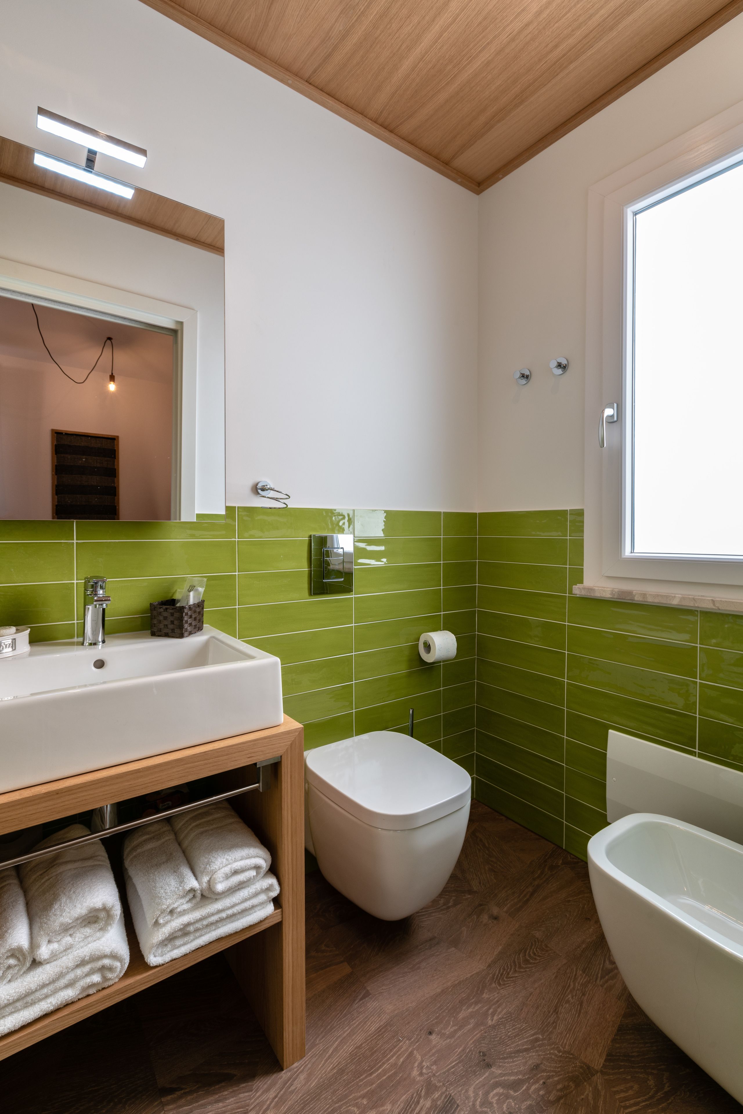 A bathroom with a wooden ceiling, green tiled walls, a white sink, a toilet, and a bathtub.